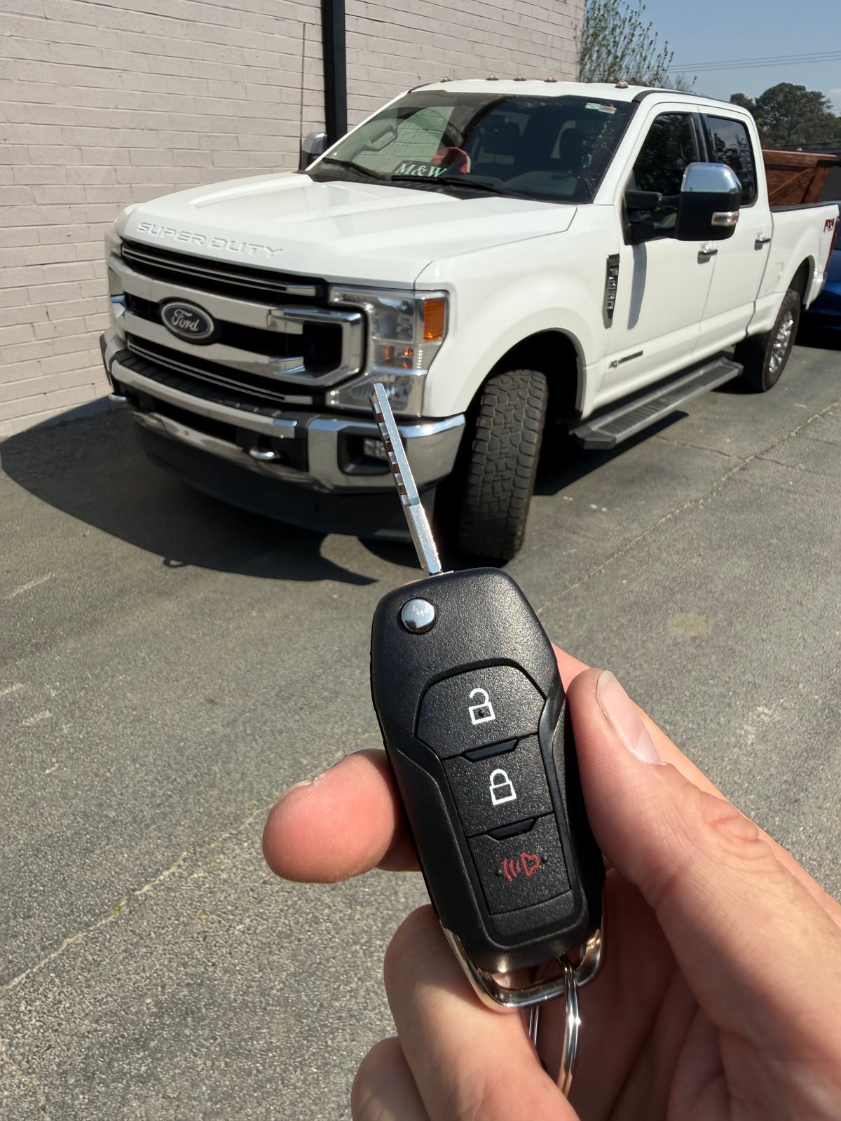 Hand holding a Ford pickup truck key fob in front of a white Ford Super Duty truck in a parking lot