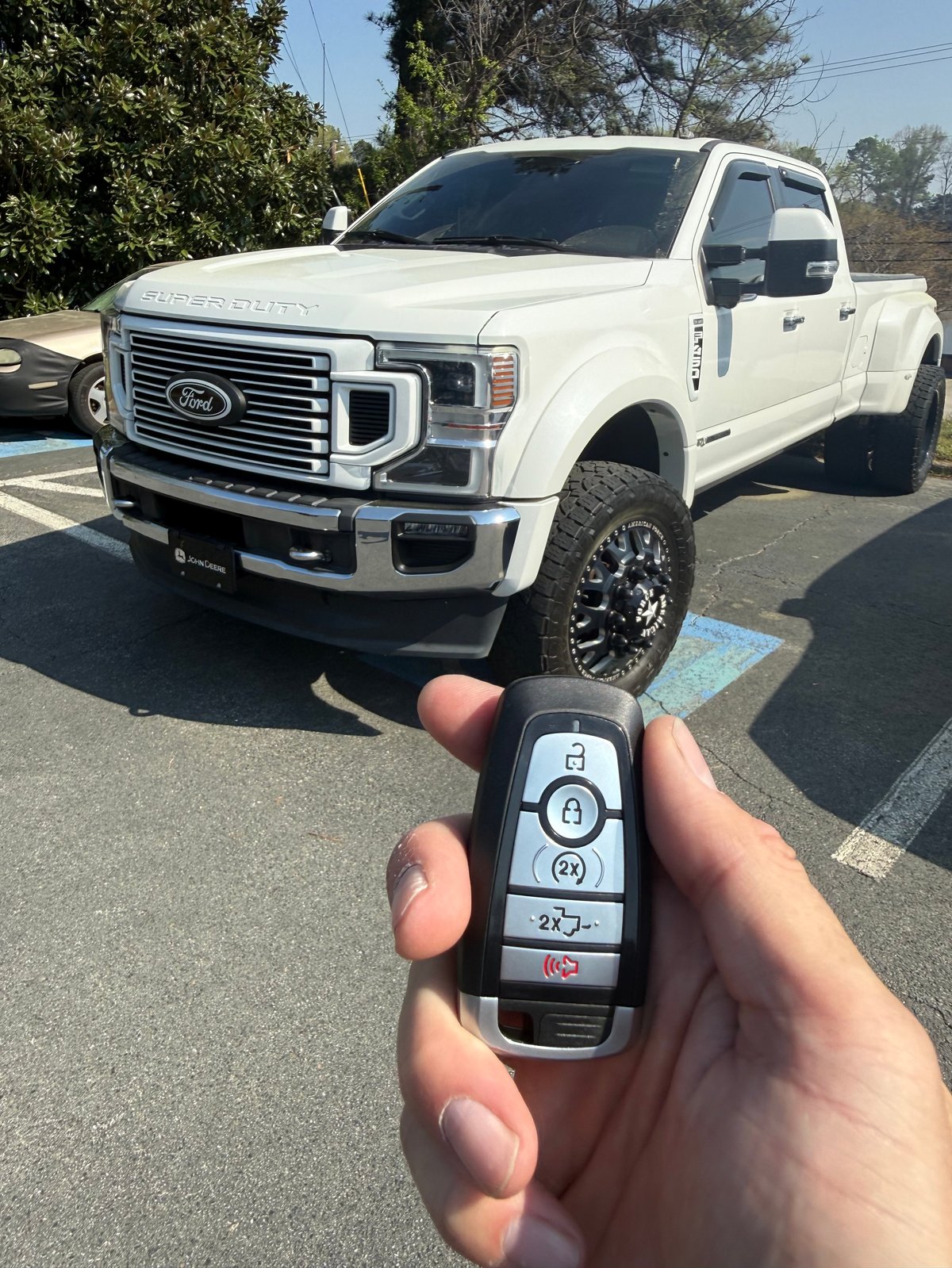 Person holding a Ford truck key fob in front of a white Ford pickup truck in a parking lot