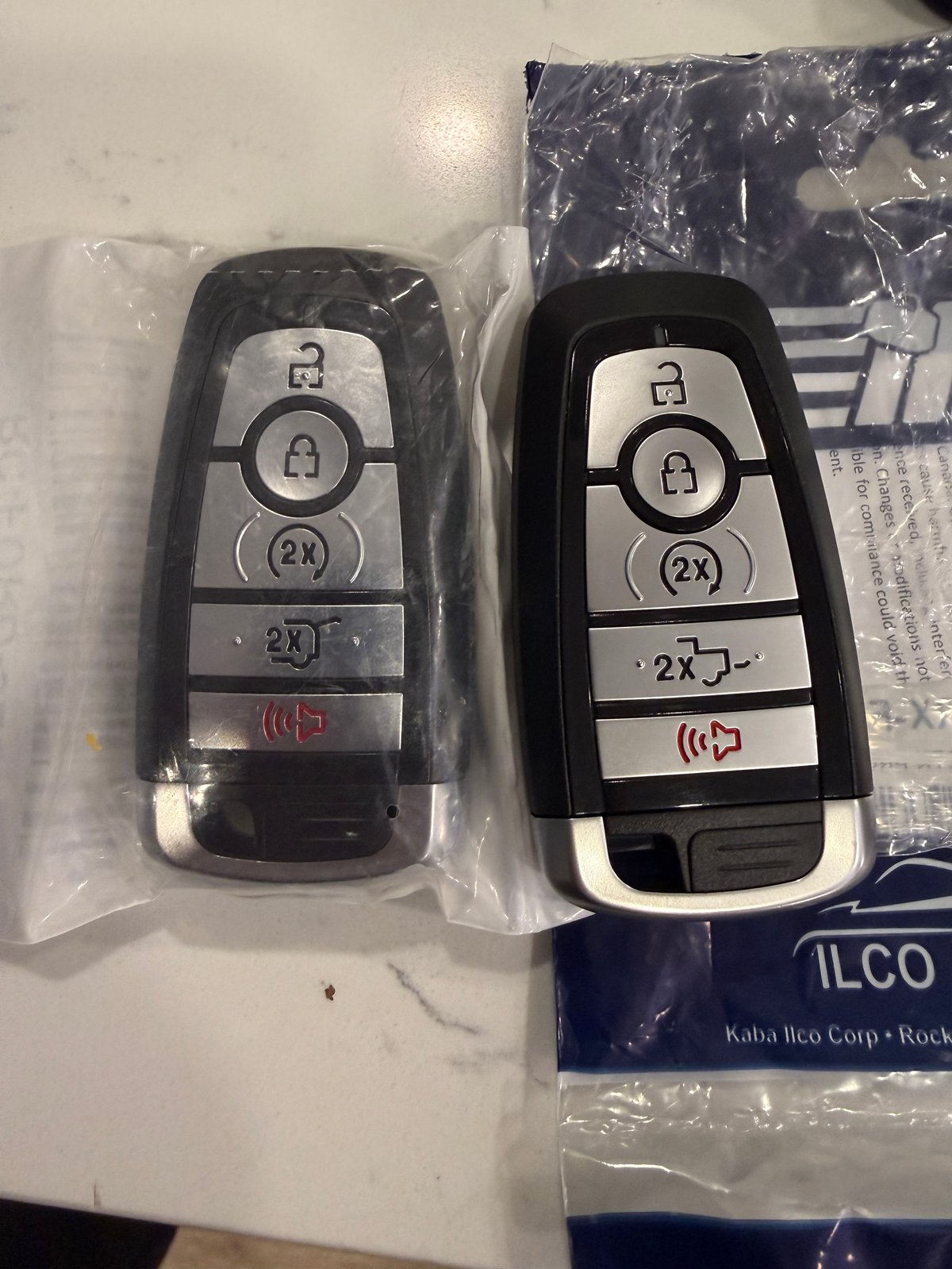Two car key fobs side by side, one black and one black with silver buttons, showing lock and unlock symbols